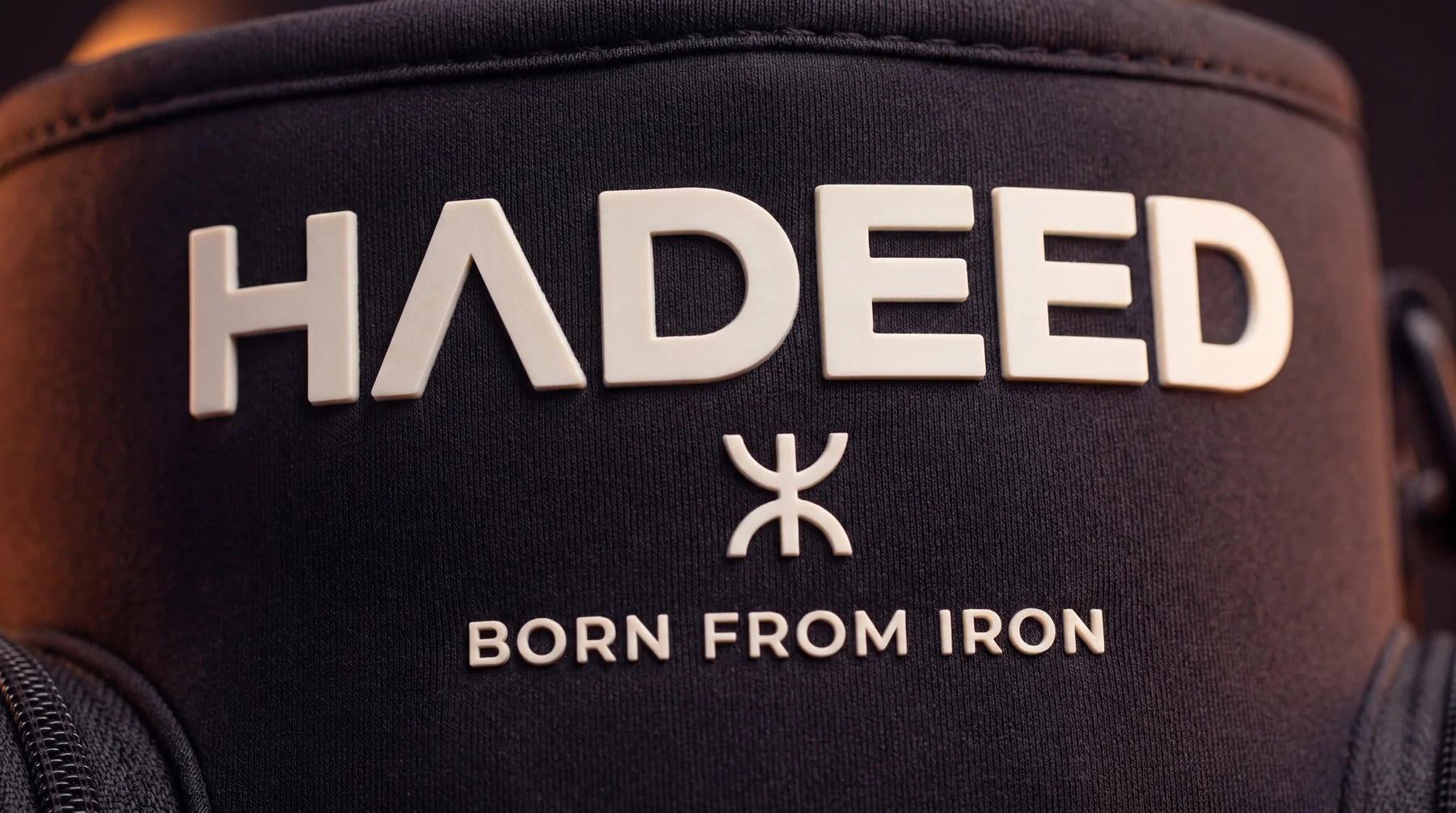 Macro detail of the HADEED logo and Aza symbol on the carrier's surface - raised silicone branding, matte finish